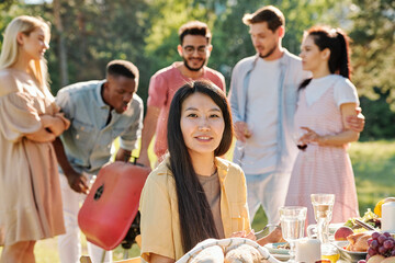 Wall Mural - Happy young Asian woman with long dark hair looking at you by served table