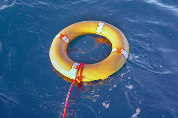 Wall Mural - Yellow lifebuoy with a rope in blue sea on water. Life ring floating on top of water. Life ring with a rope in ocean.