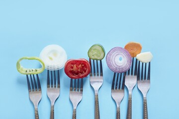 Sticker - Top view of sliced pieces of fresh vegetables and spices on forks against a blue background