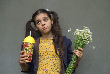 Poster - Young girl holding a bunch of daisy flowers and bottle with straw isolated on a gray background