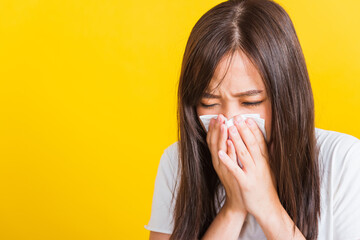 Wall Mural - Portrait of Asian beautiful young woman sad she crying wipe the mucus with tissue, Close up of pretty girl sneezing sinus using towel to wipe snot from nose, studio shot isolated on yellow background