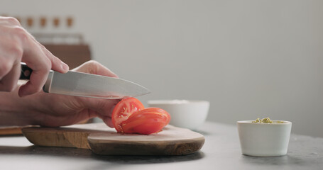 man slicing tomato on olive wood board