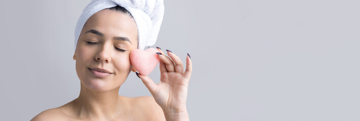 Beauty portrait of woman in white towel on head with a sponge for a body in view of a pink heart. Skincare cleansing eco organic cosmetic spa relax concept.