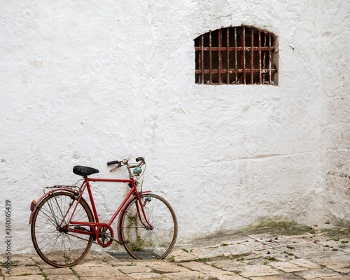 Fotomural Red bicycle leaned to a white building with a window with rusty balusters