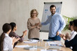 © fizkes - Smiling executive wearing glasses introducing new hired employee at corporate meeting, team leader congratulating middle aged businesswoman with job promotion, diverse colleagues applauding
