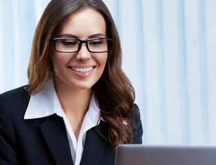 Poster - Portrait image of smiling businesswoman in black confident style suit and spectacles, working with laptop computer at office. Success in business, job and education concept.