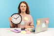 Overtime work. Exhausted fatigued upset woman employee in eyeglasses sitting at workplace office, all covered with sticky notes and holding big clock. indoor studio shot isolated on blue background