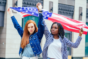 Wall Mural - lesbian redhaired ginger woman and her african american wife holding USA flag in downtown street