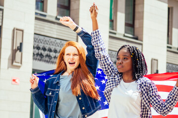 Wall Mural - lesbian redhaired ginger woman and her african american wife holding USA flag in downtown street