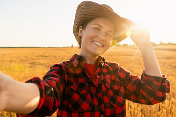 Wall Mural - Woman farmer in cowboy hat makes selfie on the background of a wheat field.