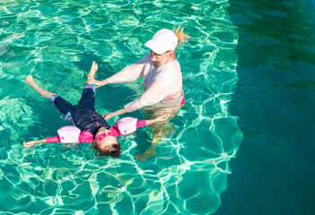 A girl, Caucasian, with a child girl 4 years old, swimming in the pool outdoors.