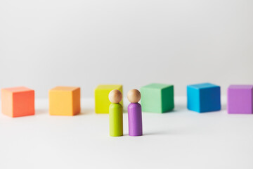 Wooden figures concept. Couple standing in front of wooden blocks in colours of the gay pride rainbow flag. Couple of white skin colour. 