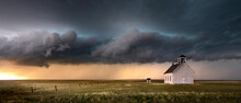Old Church In The Rural Countryside With A Sever Storm At Sunset. There Is An Outhouse Visible In The Scene As Well As A Green And Yellow Grass Meadow.