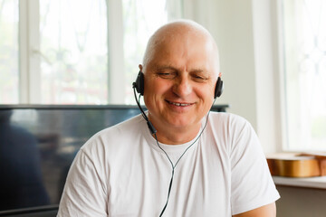 Head shot close up happy grandfather looking at camera, talking to grown up children or communicating via video call with friends, sitting on sofa at home. Pleasant old man involved in conversation.