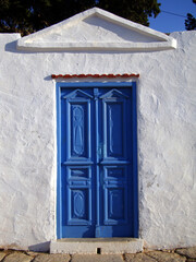 An old, indigo blue door on a white washed stone wall in the Aegean island Symi, in Greece. 