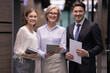 © fizkes - Smiling business people group standing together in office. Successful older businesswoman with male and female professionals looking in camera. Confident lady boss with manager and secretary