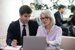 © fizkes - Mature businesswoman use laptop to discuss information with younger colleage. Experienced business woman mentor explain strategy to young manager. Two businesspeople work with online data together