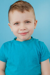 Wall Mural - Portrait of cute little boy with stylish curly hairdo in blue T-shirt standing, looking at camera with serious attentive face, calm pensive expression. indoor studio shot isolated on blue background