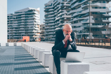 Middle age businessman sitting outdoor using computer - Concentrated professional worker connected outdoor using laptop