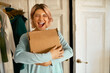 © Anatoliy Karlyuk - Indoor image of happy cheerful young woman holding cardboard box delivered to her apartment, expressing excitement, going to unpack parcel, having impatient overjoyed look. Food delivery and shopping