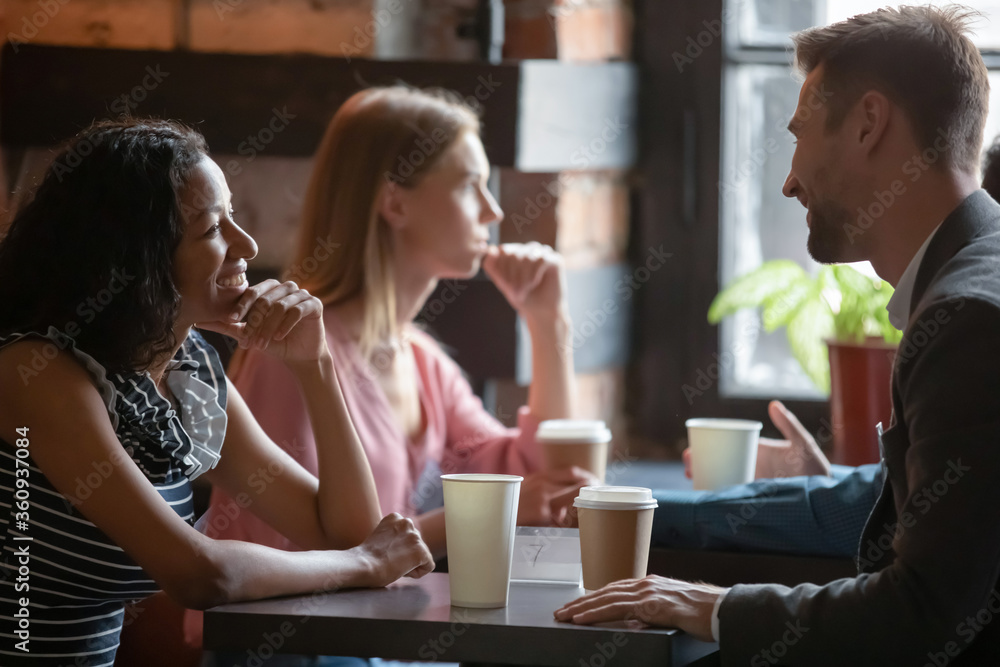Multi ethnic couples sitting in cafe enjoy chatting, focus on African girl flirting with Caucasian guy during speed dating romantic meeting participation. Love seekers, romantic relationships concept - obrazy, fototapety, plakaty 