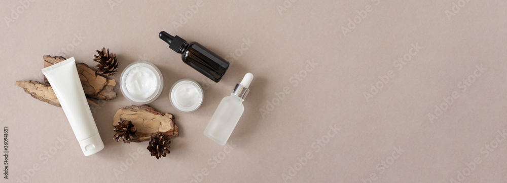 Hand, eye, facial moisturizer cream, serum, essential in glass bottles and pine bark and cone on beige background flat lay, top view. Set for skin and body care beauty products banner format - obrazy, fototapety, plakaty 