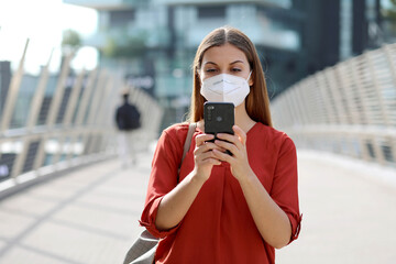 Wall Mural - Young Woman wearing KN95 FFP2 mask using smart phone app in modern city street