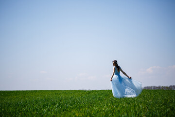 Woman in a blue long dress on a background of green field. Fashion portrait of a beautiful girl with a smile on her face