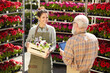 © Seventyfour - High angle portrait of smiling young woman holding box of flowers while talking to senior supervisor in plantation outdoors, copy space
