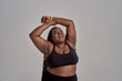 © Svitlana - Love my body. Plump, plus size african american woman in sportswear laughing, lifting her arms up in studio over grey background. Concept of sport, healthy lifestyle, body positive, equality