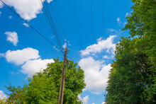 Utility Pole And Overhead Wires And Cables In A Blue Cloudy Sky In Sunlight In Summer