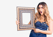 © Krakenimages.com - Young caucasian woman holding empty frame scared and amazed with open mouth for surprise, disbelief face