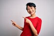 © Krakenimages.com - Young beautiful asian girl wearing casual red t-shirt standing over isolated white background smiling and looking at the camera pointing with two hands and fingers to the side.