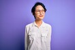 © Krakenimages.com - Young beautiful asian girl wearing casual shirt and glasses standing over purple background smiling looking to the side and staring away thinking.