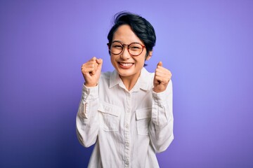 Poster - Young beautiful asian girl wearing casual shirt and glasses standing over purple background excited for success with arms raised and eyes closed celebrating victory smiling. Winner concept.