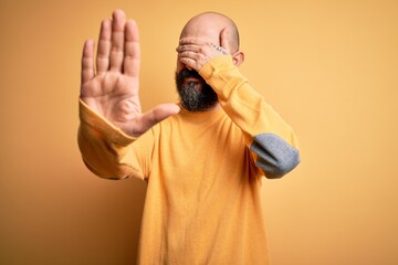 Poster - Handsome bald man with beard wearing casual sweater standing over yellow background covering eyes with hands and doing stop gesture with sad and fear expression. Embarrassed and negative concept.