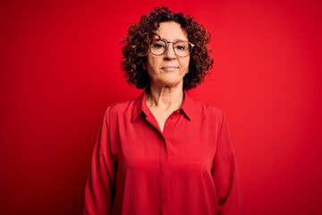 Poster - Middle age beautiful curly hair woman wearing casual shirt and glasses over red background looking sleepy and tired, exhausted for fatigue and hangover, lazy eyes in the morning.