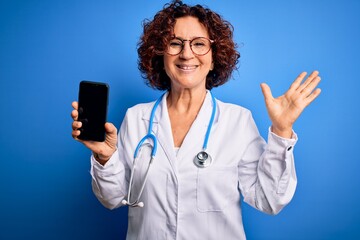 Sticker - Middle age doctor woman wearing coat and stethoscope holding smartphone showing screen very happy and excited, winner expression celebrating victory screaming with big smile and raised hands