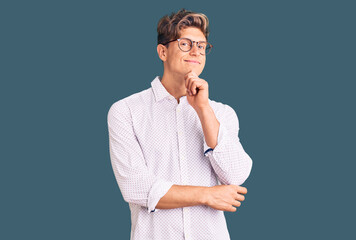 Young handsome man wearing business clothes and glasses looking confident at the camera smiling with crossed arms and hand raised on chin. thinking positive.