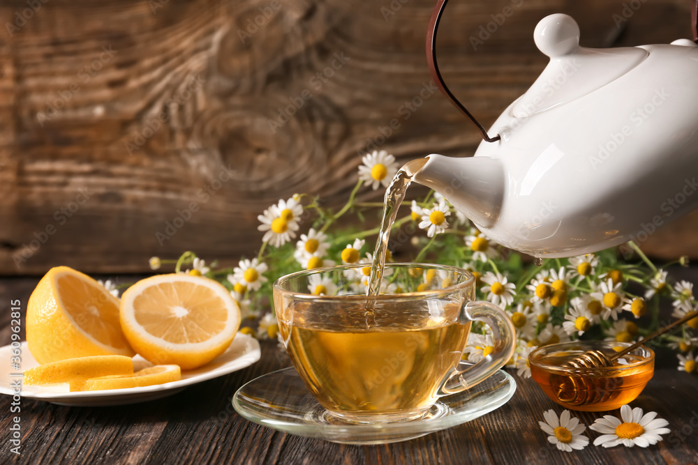 Pouring of chamomile tea from teapot into cup on table