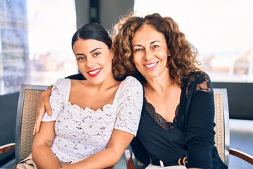 Beautiful mother and daughter smiling happy and confident. Sitting with smile on face hugging at restaurant