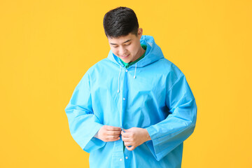 Wall Mural - Young Asian man in raincoat on color background