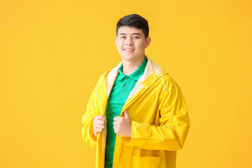 Wall Mural - Young Asian man in raincoat on color background