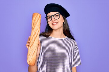 Poster - Young beautiful girl wearing fashion french beret holding fresh baked bread baguette with a happy face standing and smiling with a confident smile showing teeth