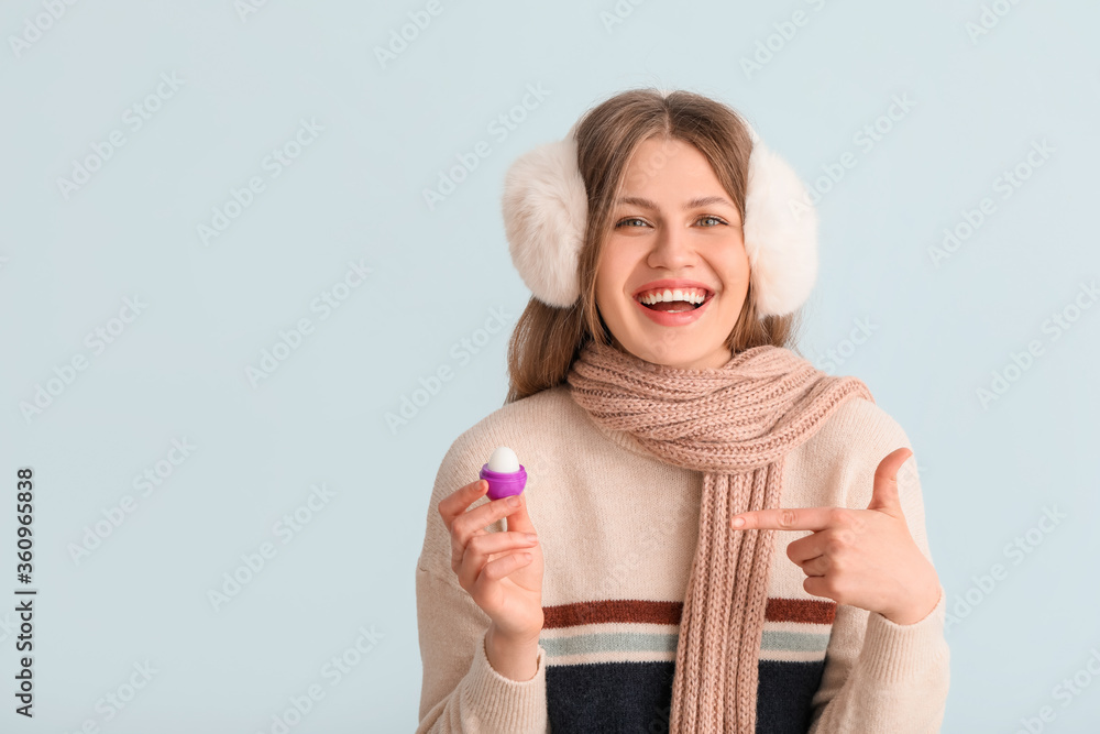 Beautiful young woman with lip balm on light background