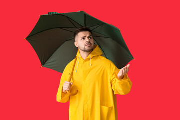 Wall Mural - Young man in raincoat and with umbrella on color background