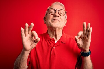 Canvas Print - Grey haired senior man wearing glasses and casual t-shirt over red background relax and smiling with eyes closed doing meditation gesture with fingers. Yoga concept.