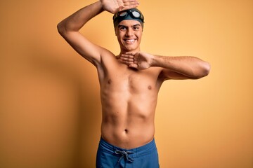 Poster - Young handsome man shirtless wearing swimsuit and swim cap over isolated yellow background Smiling cheerful playing peek a boo with hands showing face. Surprised and exited