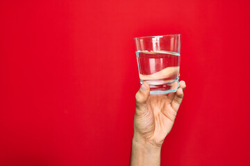 Wall Mural - Beautiful hand of man holding glass of water over isolated red background