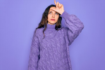 Wall Mural - Young beautiful woman wearing casual turtleneck sweater standing over purple background making fun of people with fingers on forehead doing loser gesture mocking and insulting.